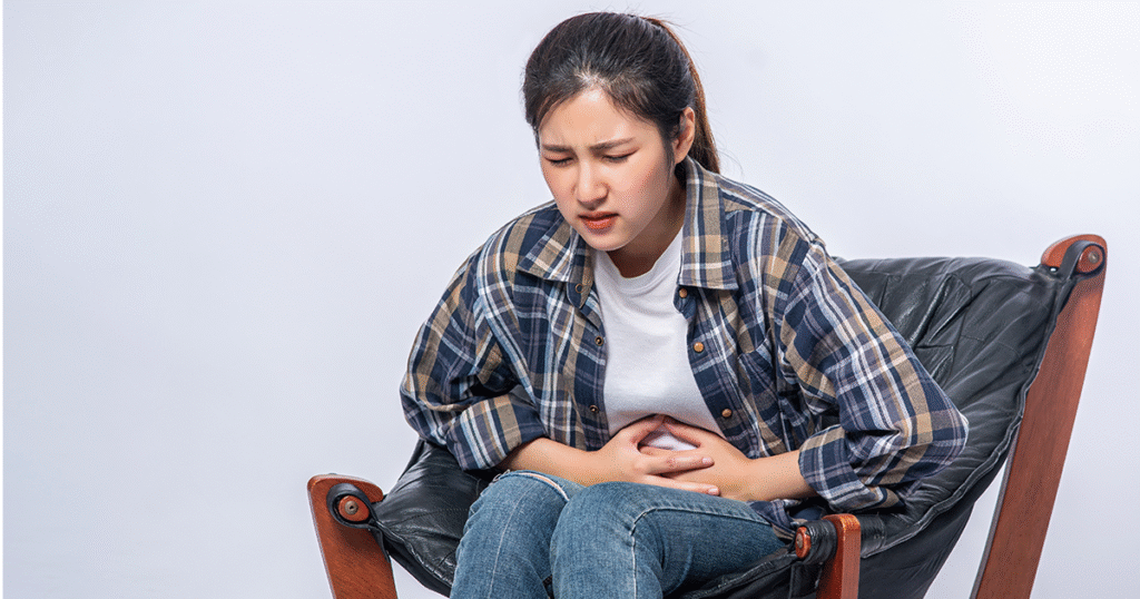 A woman sitting on a chair, visibly distressed, experiencing abdominal pain from stress.