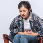 A woman sitting on a chair, visibly distressed, experiencing abdominal pain from stress.