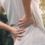 A man is grasping his back, showing signs of discomfort related to middle of back pain.