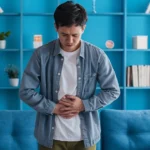 Person holding stomach experiencing stomach ache at home indoors.