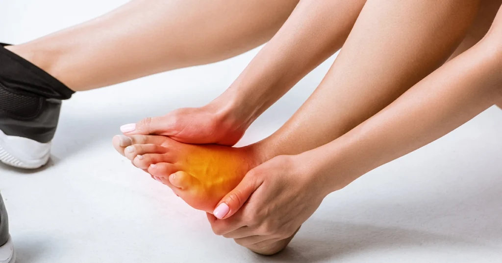 Person holding top of foot experiencing pain and inflammation