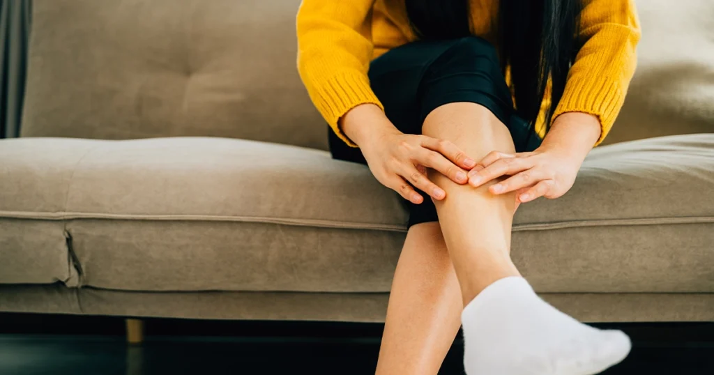 Person holding aching leg while sitting at home night.