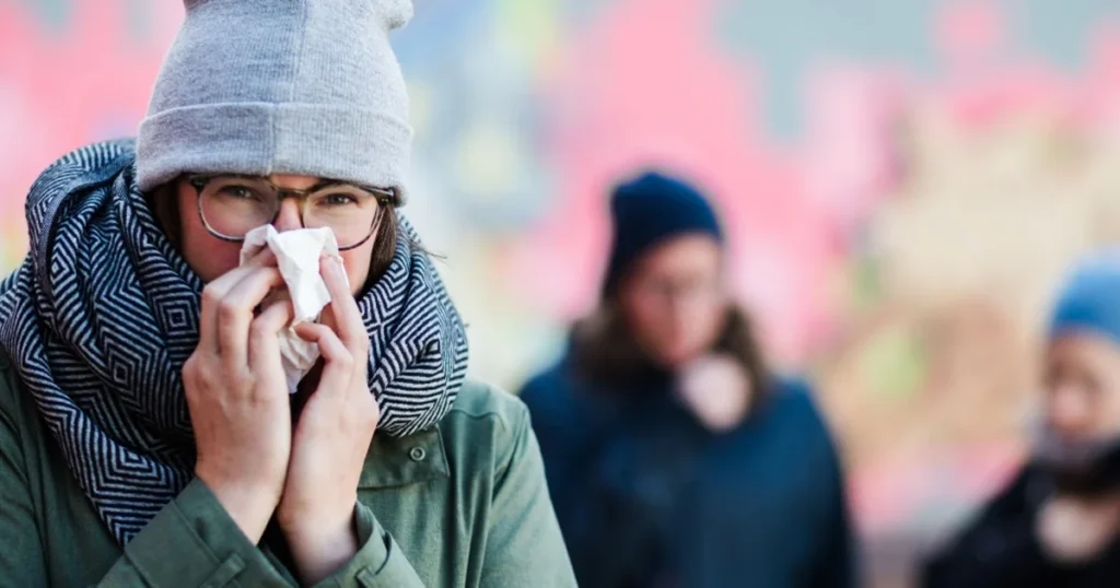 Person in winter gear blowing their nose, illustrating walking pneumonia symptoms