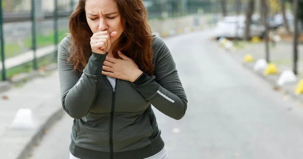 Woman outdoors clutching her chest and coughing due to walking pneumonia.
