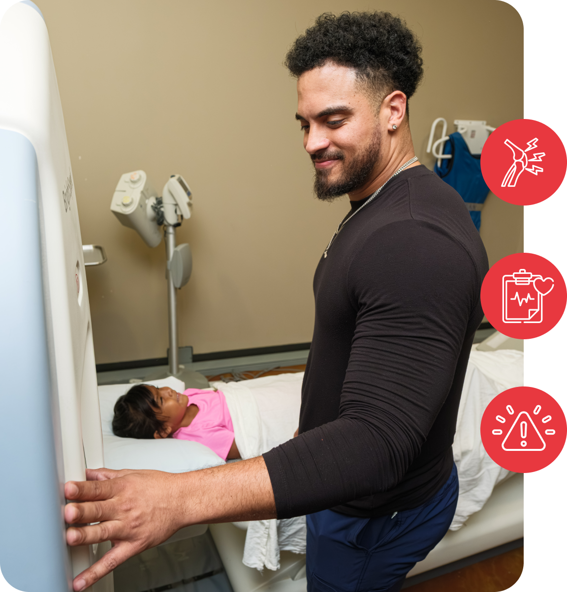 A man operates medical equipment beside a young patient in a hospital room, smiling.