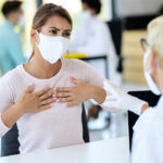 A woman in a mask and gloves speaks with a doctor in an ER setting in Texas.
