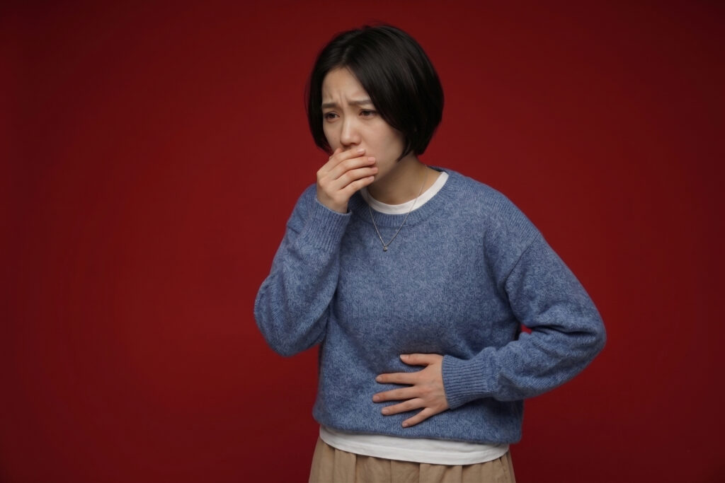 Woman in blue sweater with hand over mouth and stomach, showing nausea and discomfort on a dark red background.