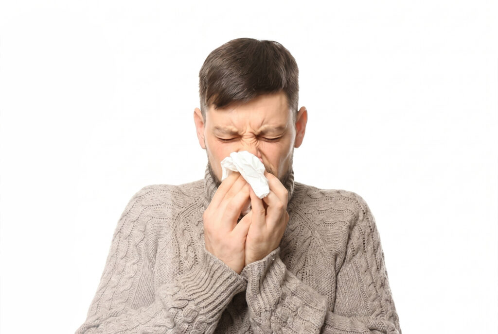 A man in a sweater blowing his nose into a tissue due to allergy.