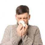 A man in a sweater blowing his nose into a tissue due to allergy.