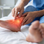 A patient in a hospital bed, grimacing in pain, with a focus on their affected foot.