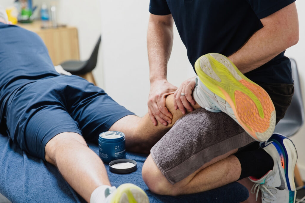 A physical therapist massages the calf of a patient lying face down on a treatment table.