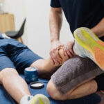 A physical therapist massages the calf of a patient lying face down on a treatment table.