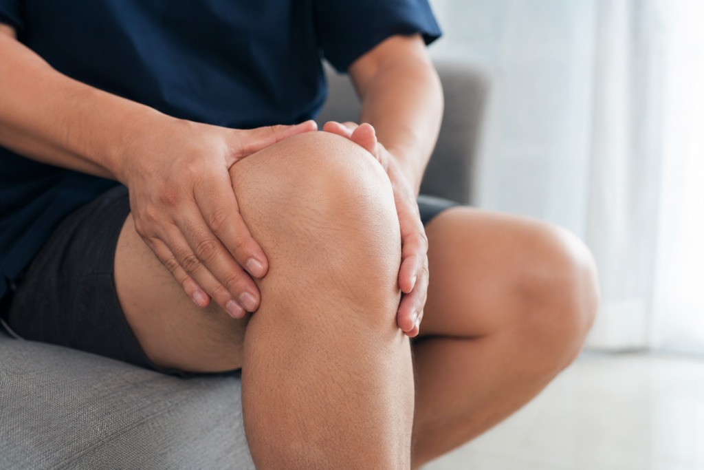 Realistic person holding swollen knee while sitting indoors with visible discomfort